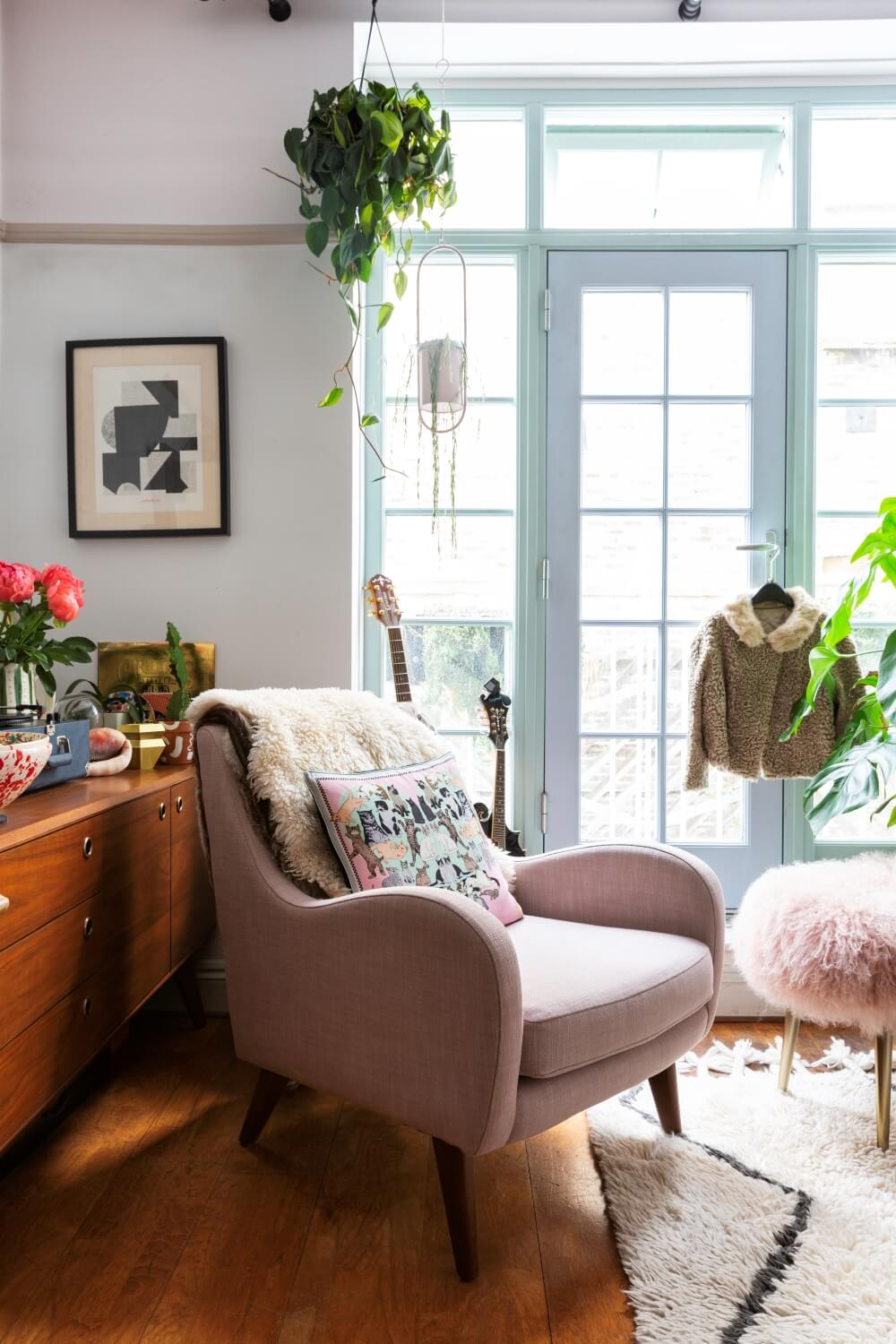 pink arm chair in front of large pale blue windows in listed property. Indoor plants suspended from curtain rails