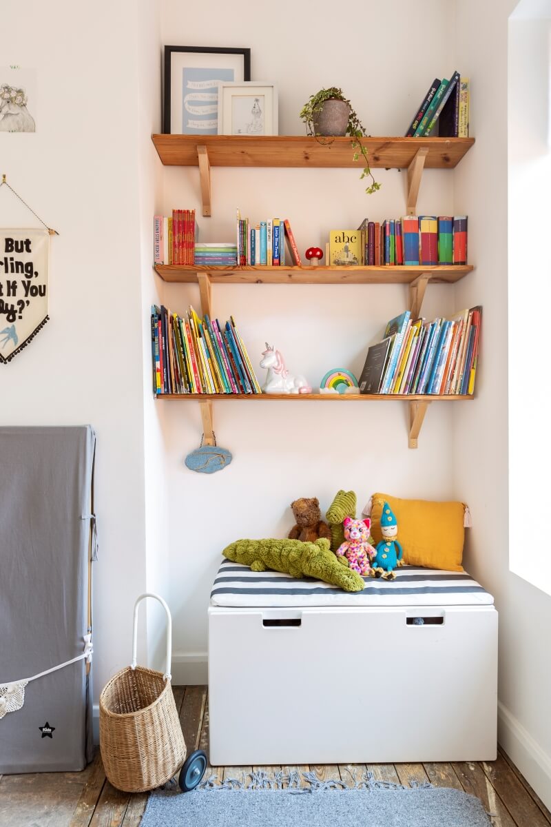 Wall shelves in alcove of rented kids room with ikea storage seat underneath. Shelves contain childrens books. 