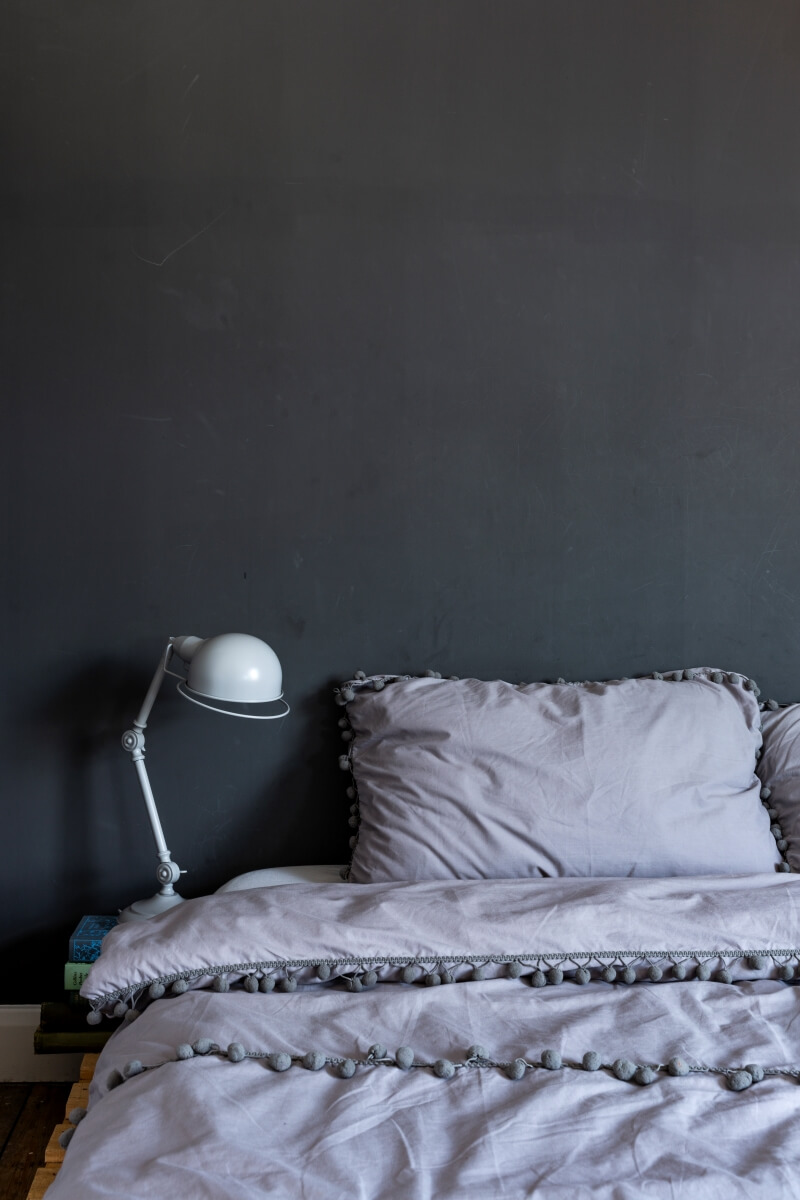Pallet bed against a dark grey wall. Grey pom pom bedding on the bed