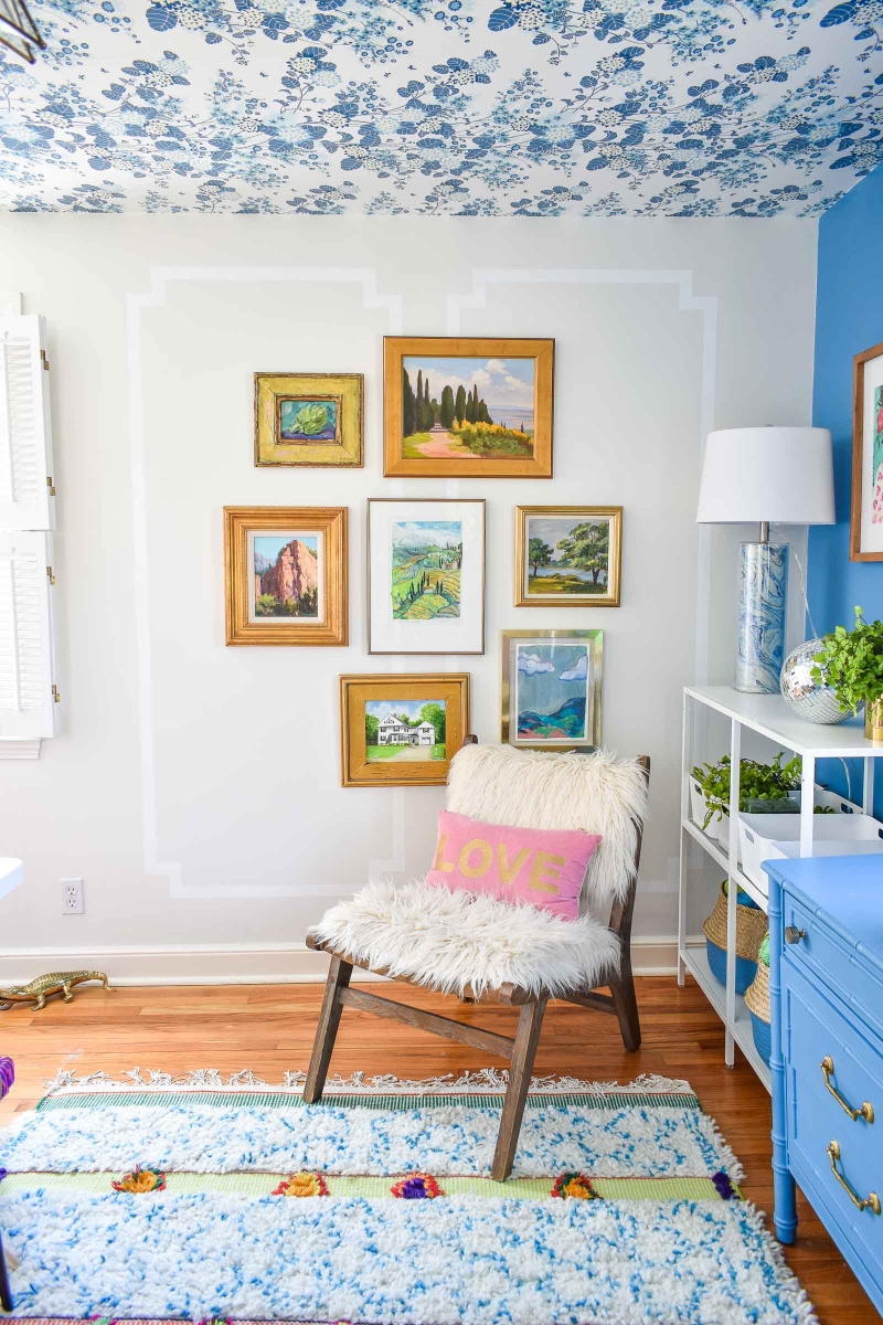 Gallery wall  behind a white chair with a wallpapered ceiling