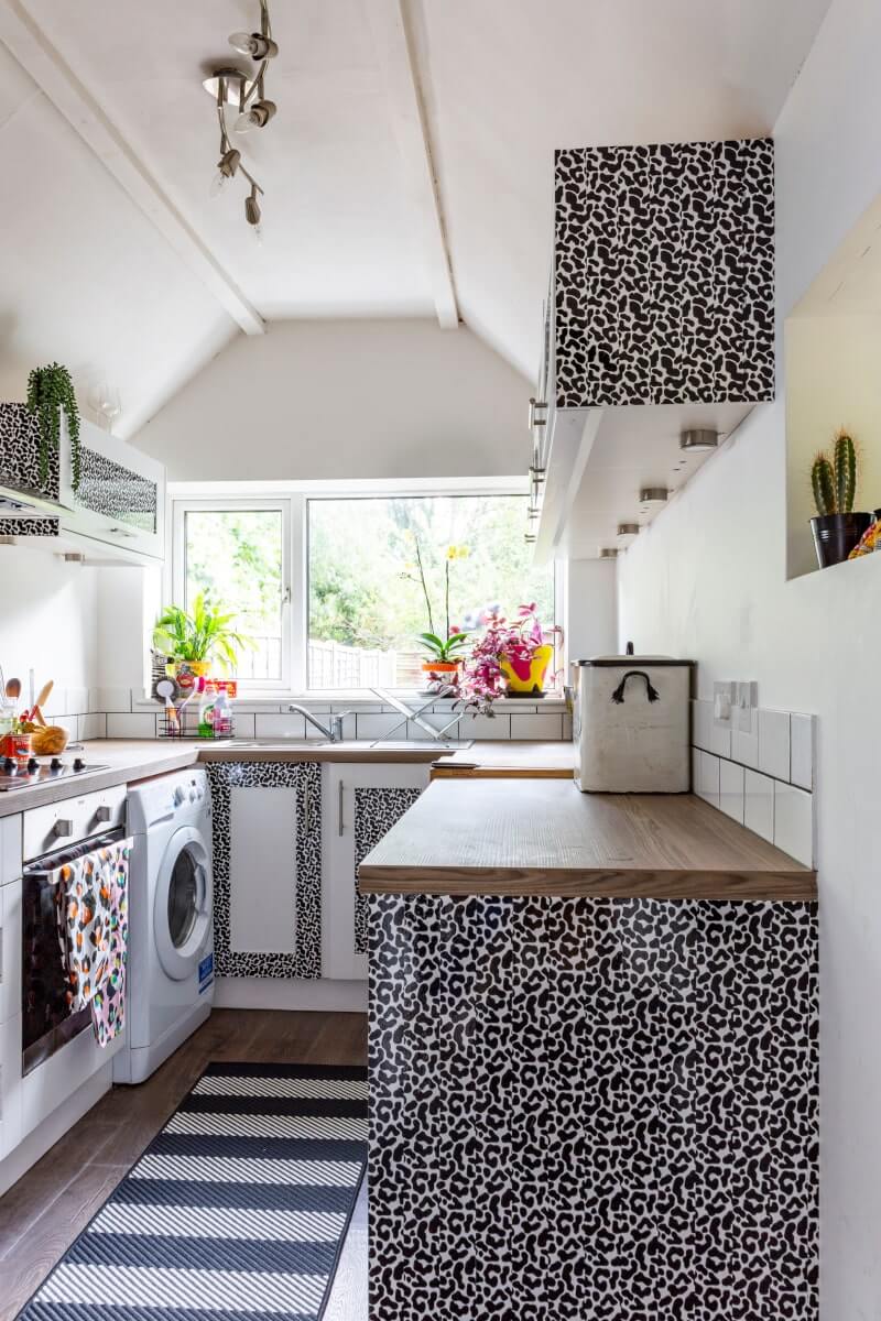 Under cabinet lighting in a leopard vinyl rented apartment small kitchen, a striped rug on the floor 